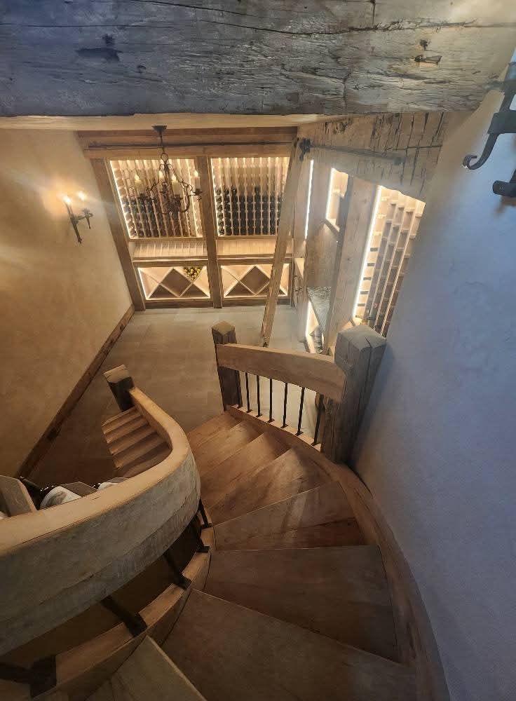 Wooden spiral staircase leading down to a wine cellar with visible wine racks and lighting.