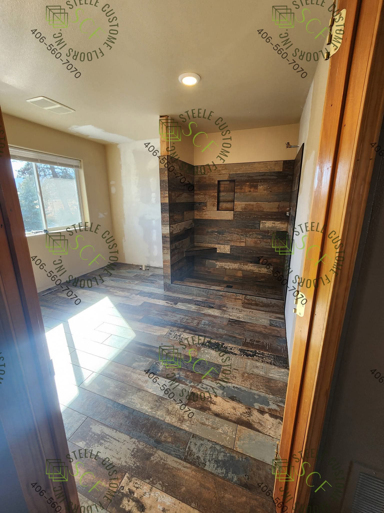 Bathroom with wood-look tile flooring and shower. The shower wall has wood paneling. Window on the left.