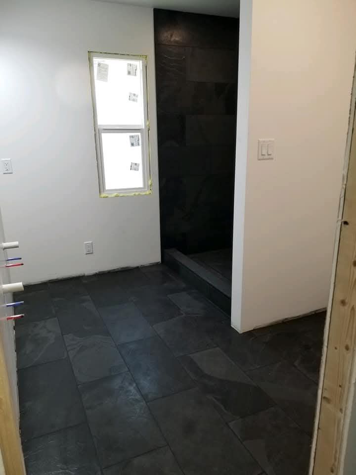 Bathroom renovation with black tiled floor and shower, white walls, and a small window.