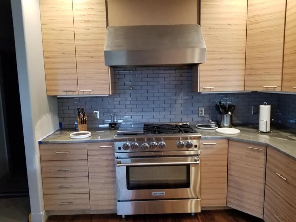 Modern kitchen with stainless steel appliances, light wood cabinets, and gray tile backsplash.