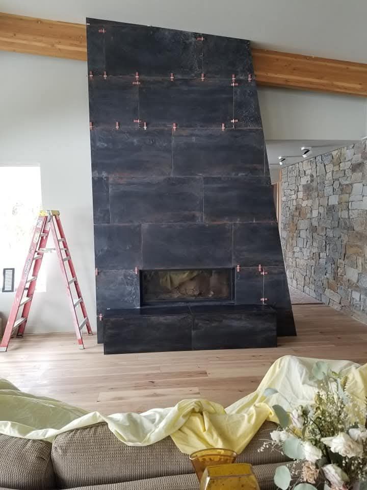 Fireplace with dark stone tiling under construction; red ladder, wood floor and ceiling beams visible.
