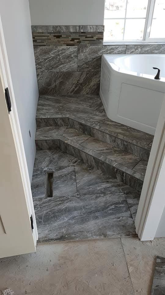 Bathroom with tiled steps leading up to a bathtub; gray and white color scheme.