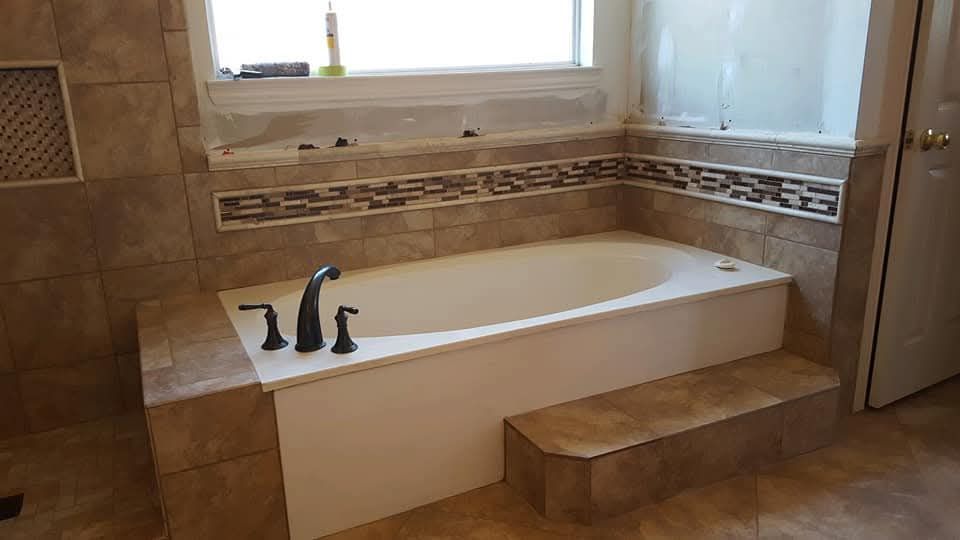Bathroom with a built-in white bathtub, tan tile surround, and decorative mosaic tile trim.