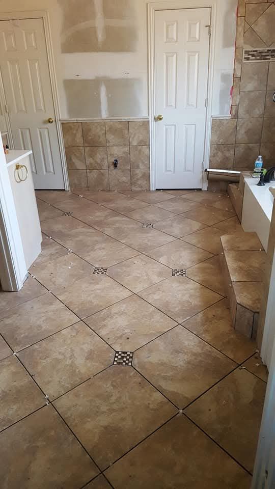 Person tiling a floor, using a trowel to spread mortar. Tools and tiles are present.
