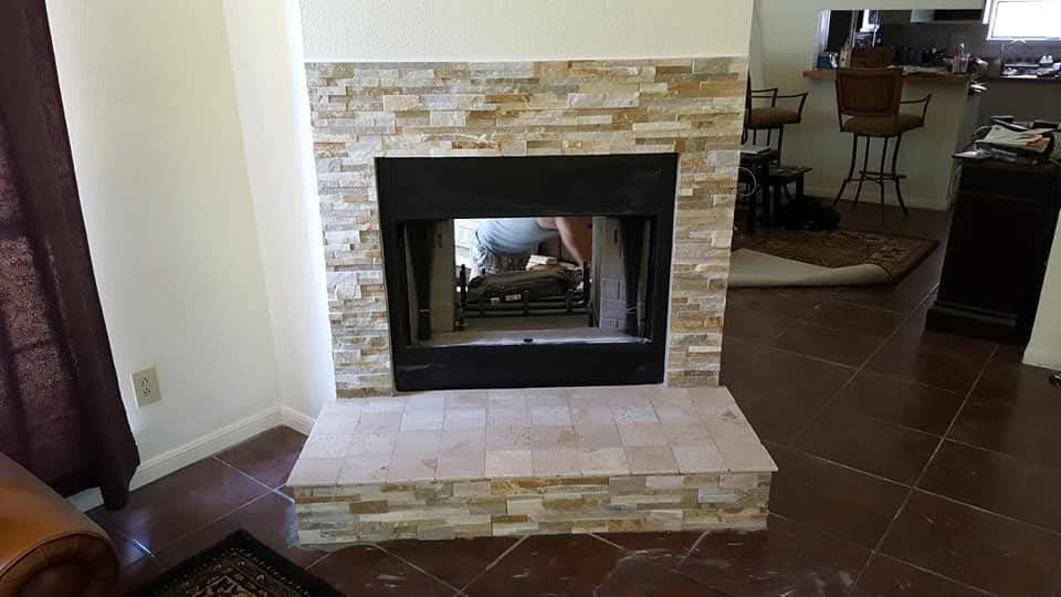 Fireplace with stone facade, dark surround, and light tile hearth in a home interior.