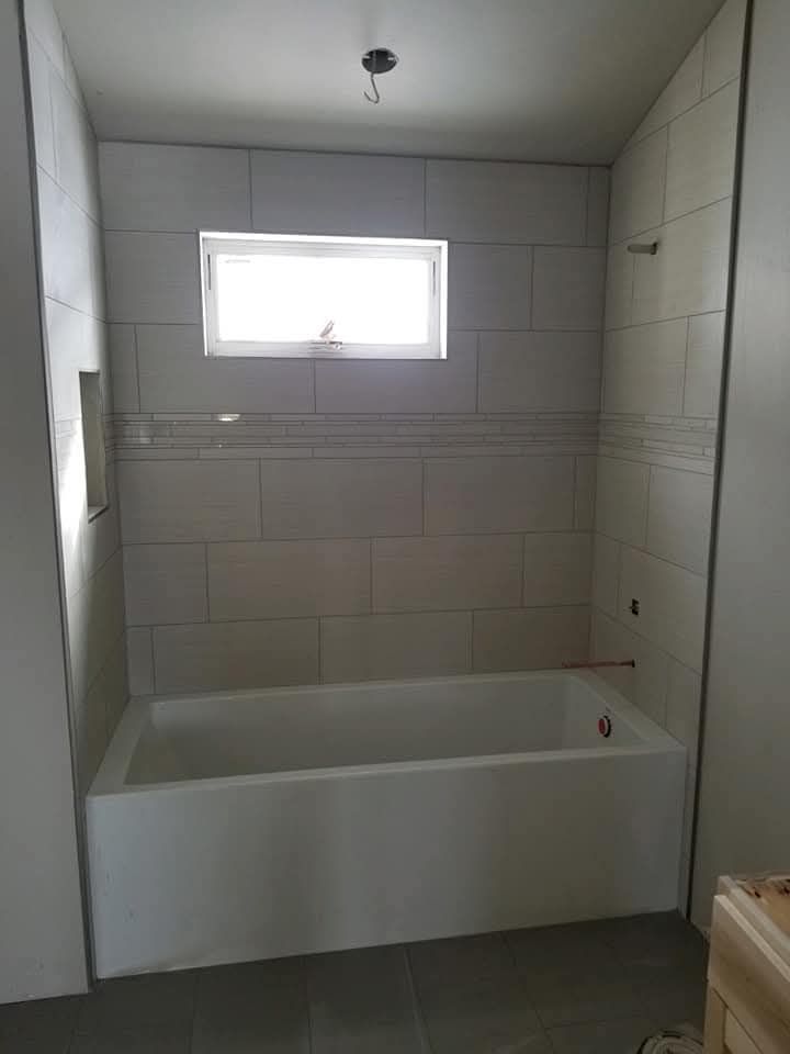 Bathroom with white bathtub, tiled walls, small window, and unfinished drywall.