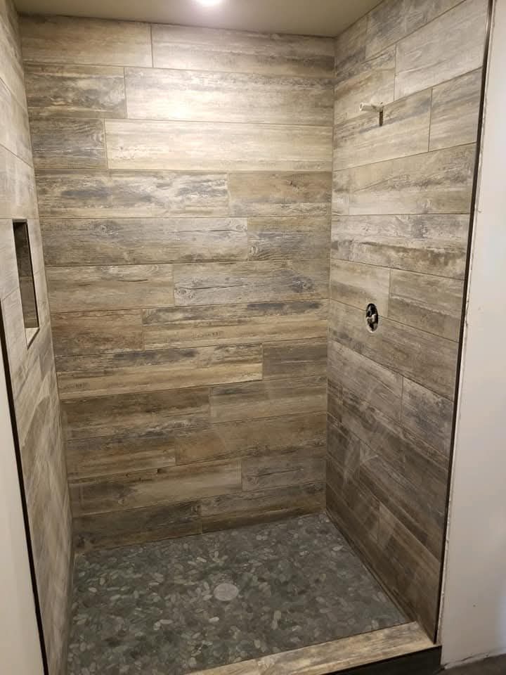 Shower with wood-look tile walls, pebble floor, and recessed shelf.