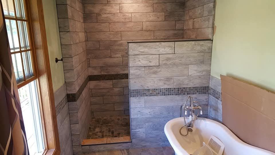 Bathroom with stone-like tile shower, built-in bench, claw-foot tub, and window.