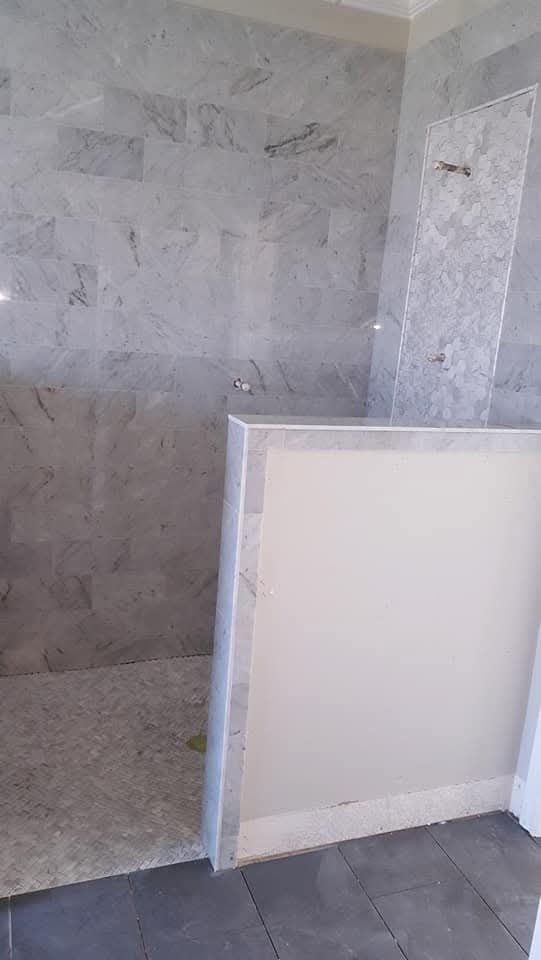 Bathroom shower with marble tile walls and floor, and a partial wall.