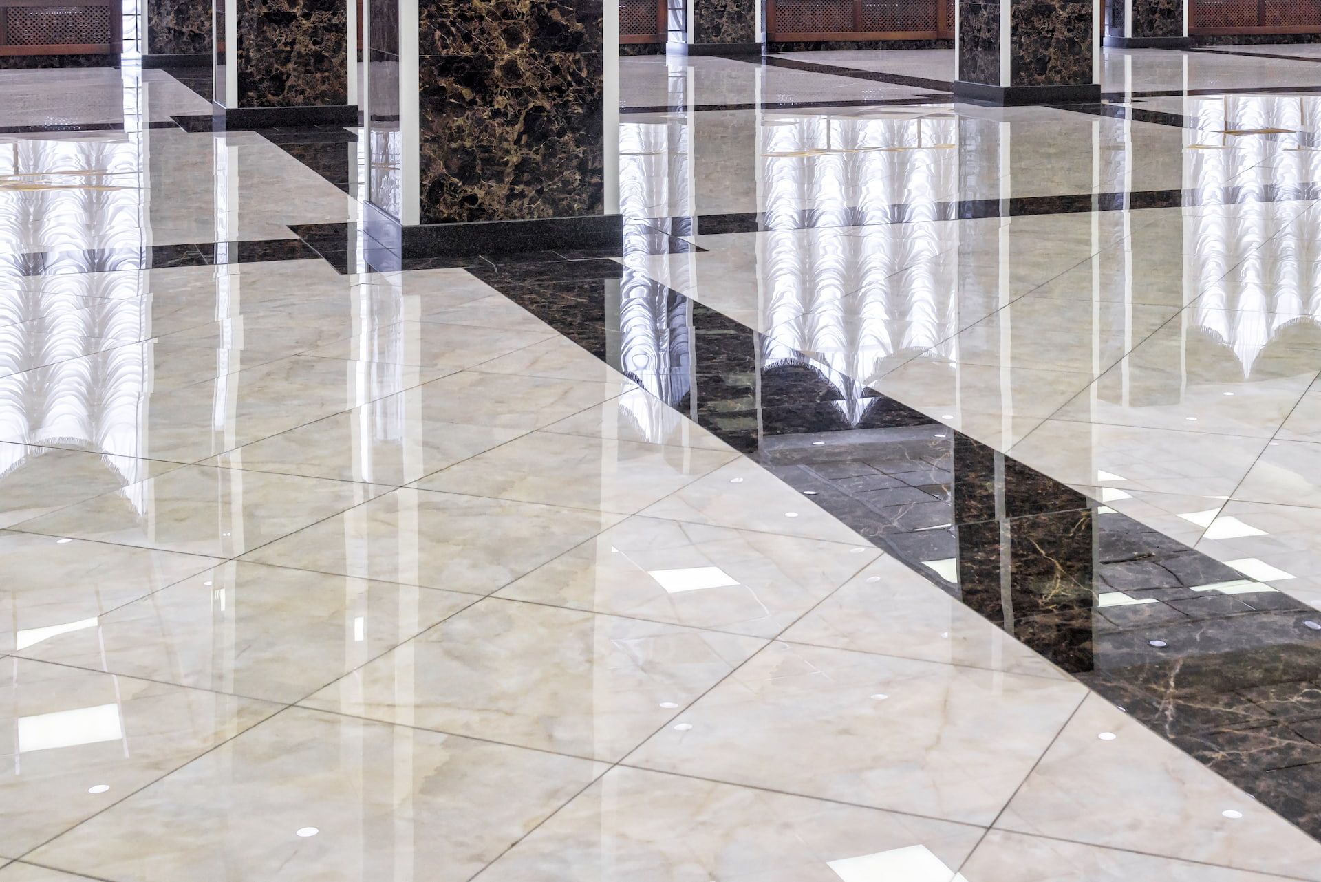 Polished, light-colored square floor tiles accented by a dark, marbled diagonal stripe and reflective marble columns.