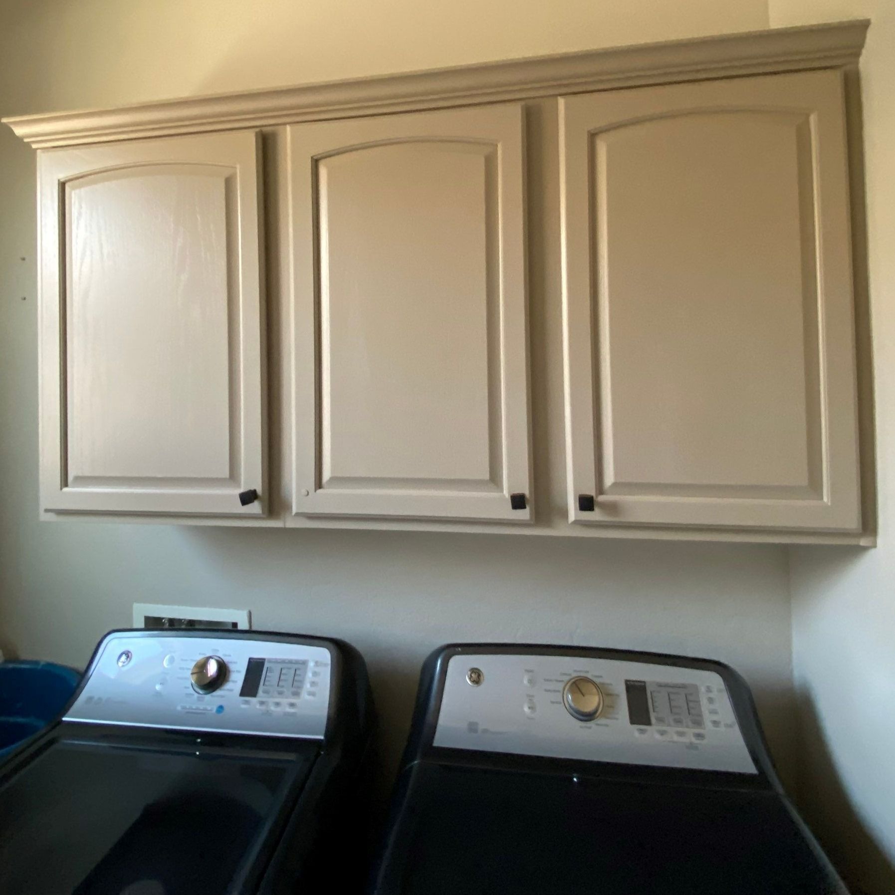 Beige cabinets above black washer and dryer in a laundry room.