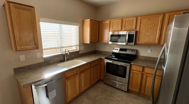 Kitchen with light brown cabinets, stainless steel appliances, and a window with blinds.