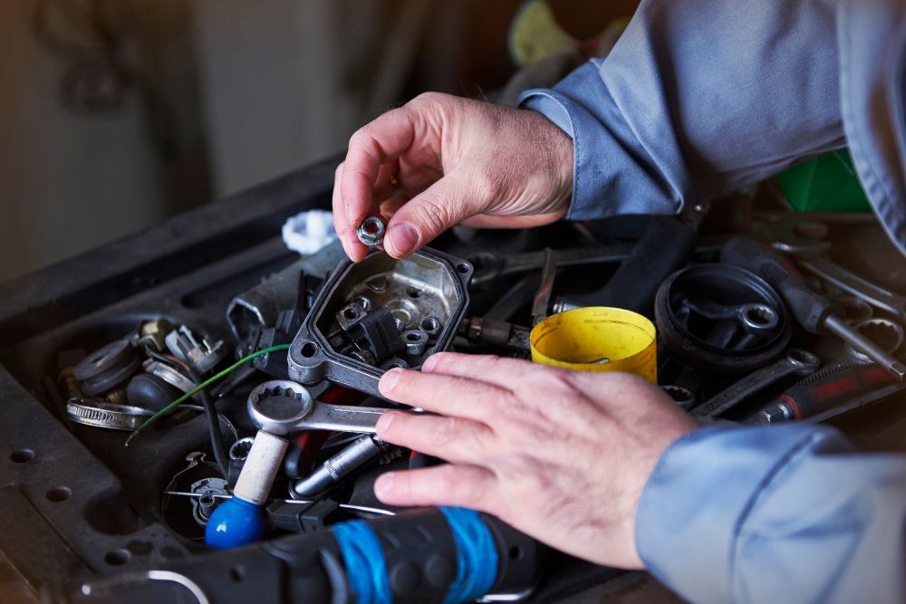 Hands working on a cluttered workbench with tools and mechanical parts