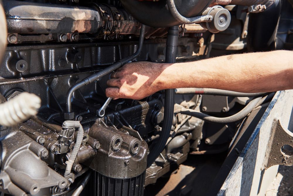 Hand reaching into the engine compartment of a vehicle, inspecting mechanical parts under the hood.