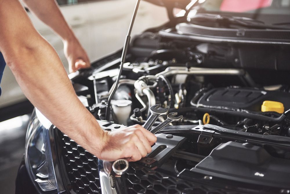 Mechanic tightening bolts in an open car engine bay