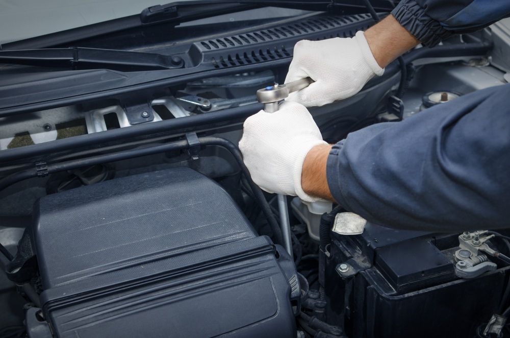 Mechanic using a wrench to work on a car engine in an open hood compartment