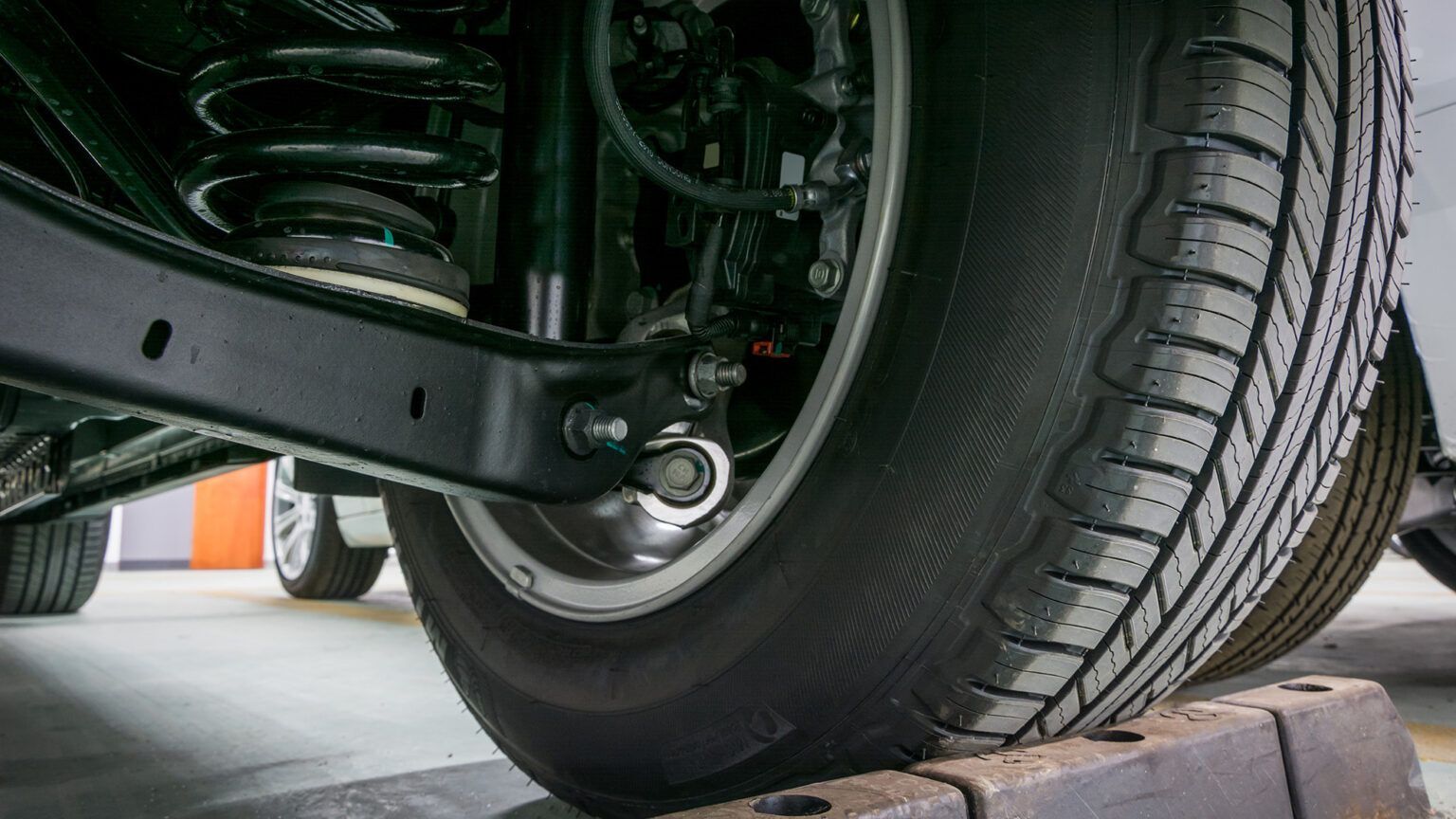 Close-up of a car wheel and suspension on a tire, shown on a lift in a garage.