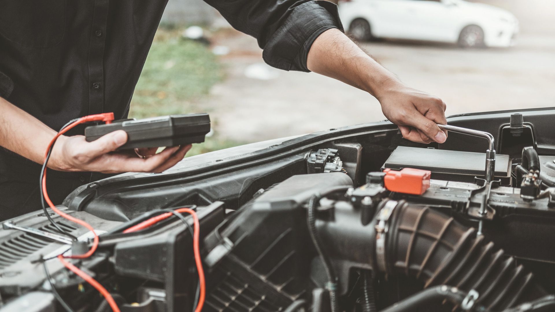 Person using a multimeter to inspect a car engine with the hood open.