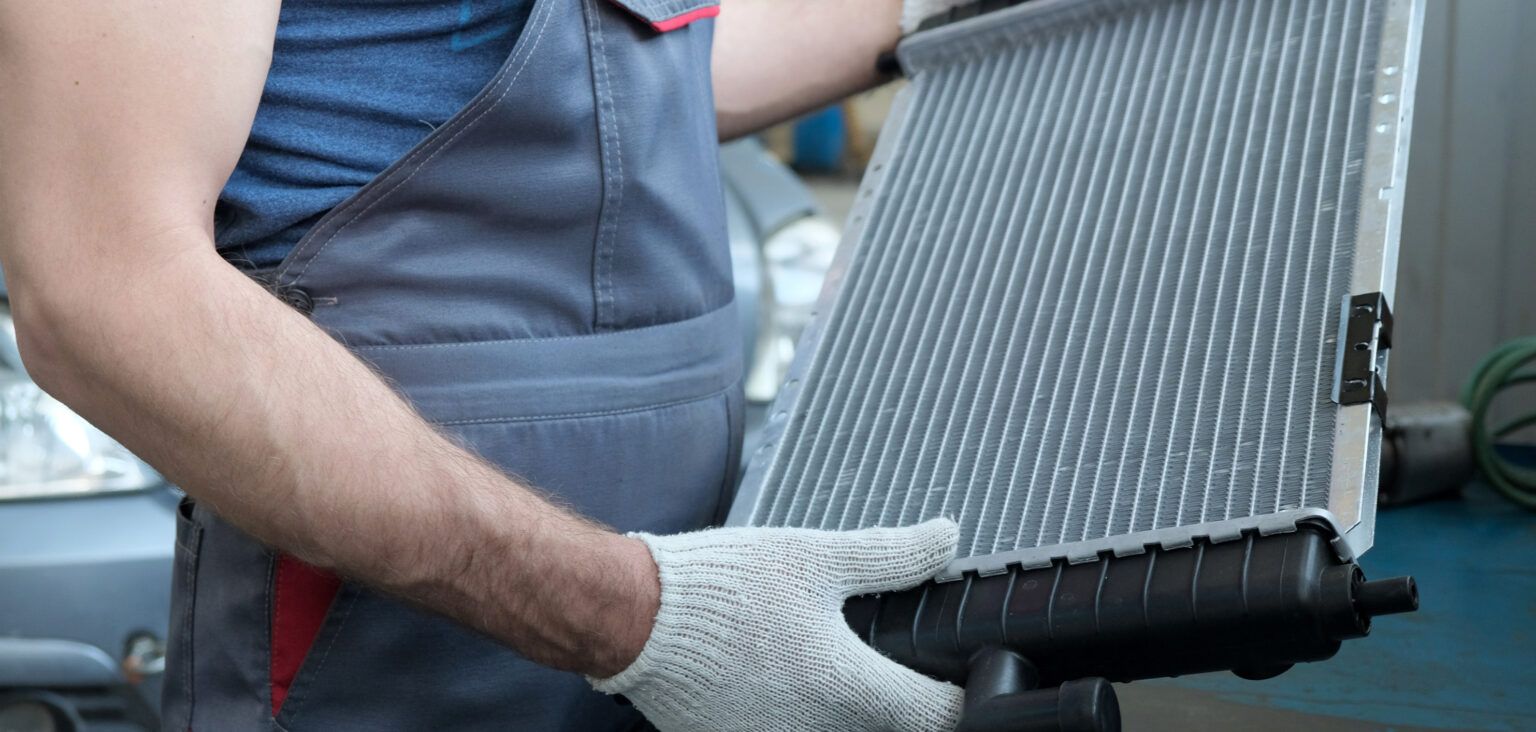 Worker in gloves handling a large car radiator or cooling panel in a workshop