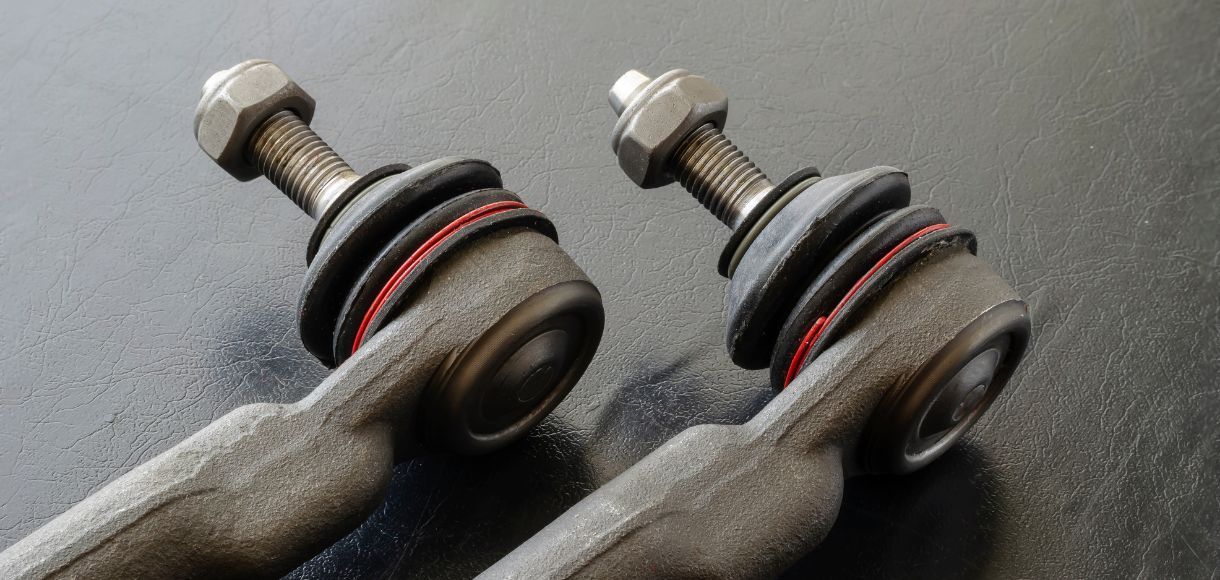 Close-up of two metal suspension ball joints with nuts and red dust boots on a dark surface