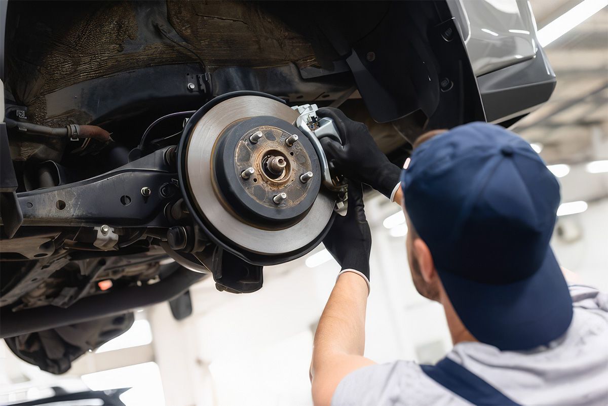 Mechanic inspecting a carβs exposed wheel brake assembly with a wrench in a garage