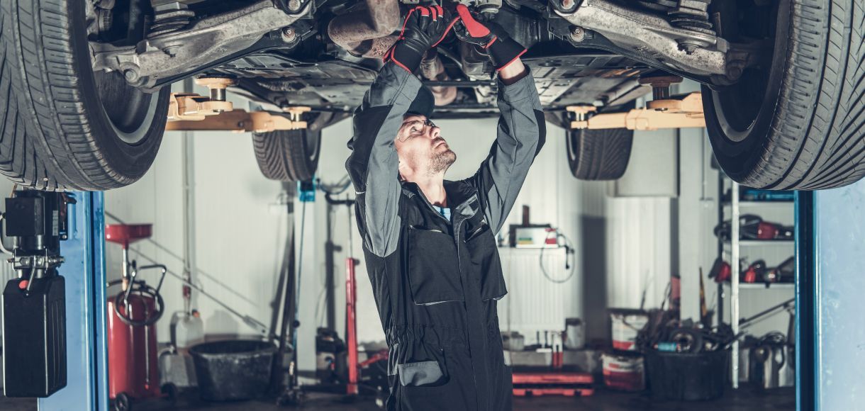 Mechanic working under a raised car in an auto repair garage, inspecting the undercarriage.