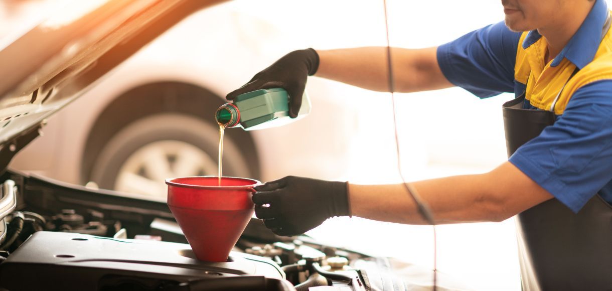 Mechanic pouring oil into a car engine with a red funnel in a garage
