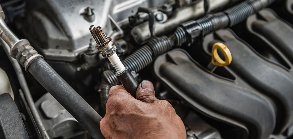 Hand using a spark plug wrench to service an engine with black hoses and parts