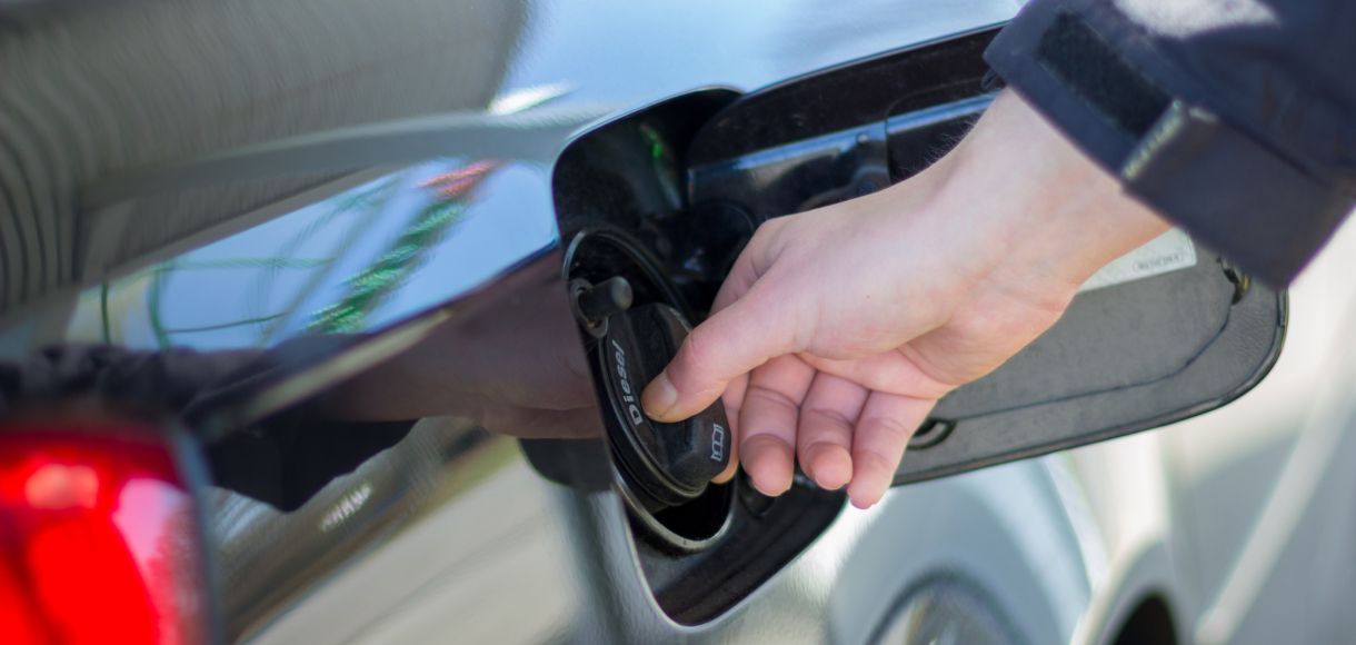Hand refueling a black car at a gas pump, close-up of the nozzle and fuel filler cap