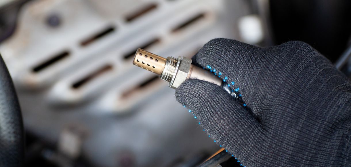 Gloved hand holding a metal spark plug near an engine bay