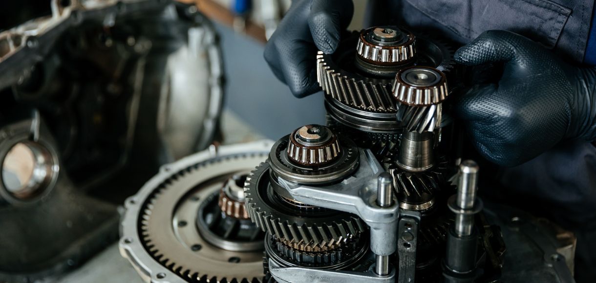 Gloved mechanic repairing a car transmission with exposed gears in a workshop