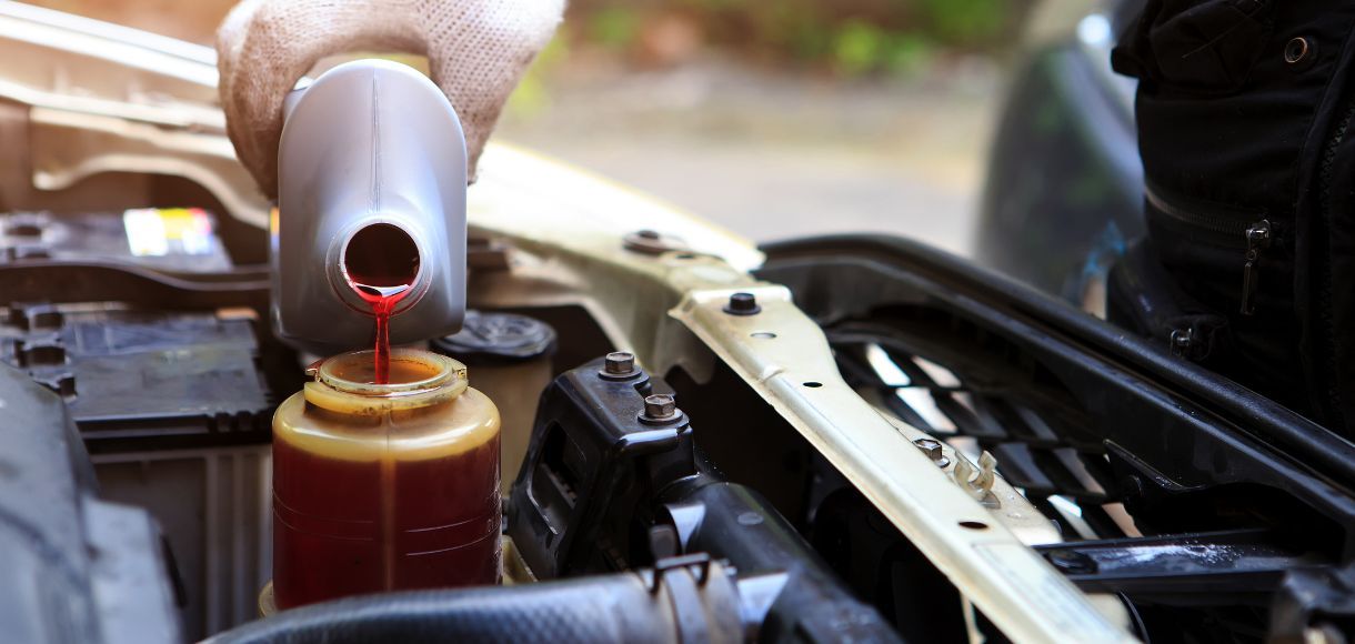 Oil being poured from a metal spout into a car engine reservoir