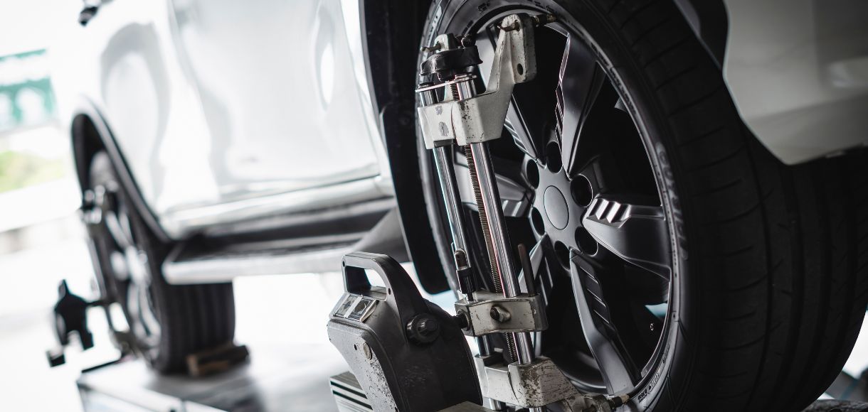 Car jack lifting a white car, close-up of wheel and undercarriage in a garage