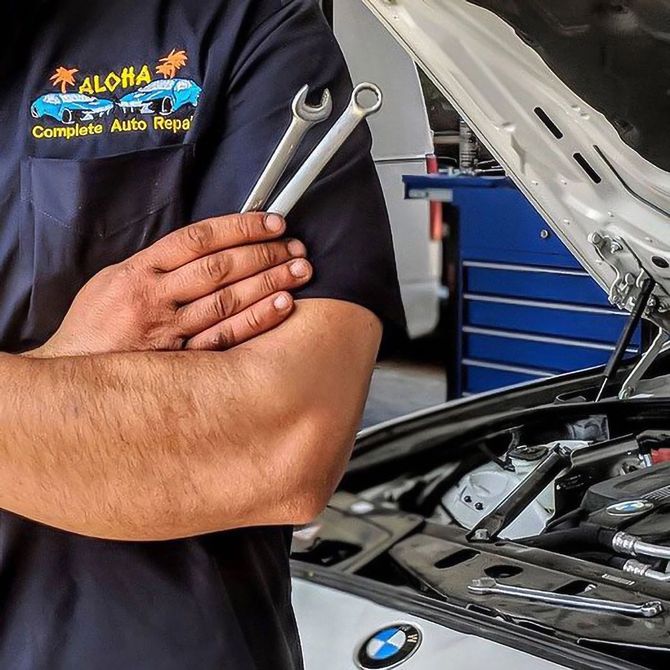 Mechanic in black shirt with crossed arms beside a BMW in an auto repair shop