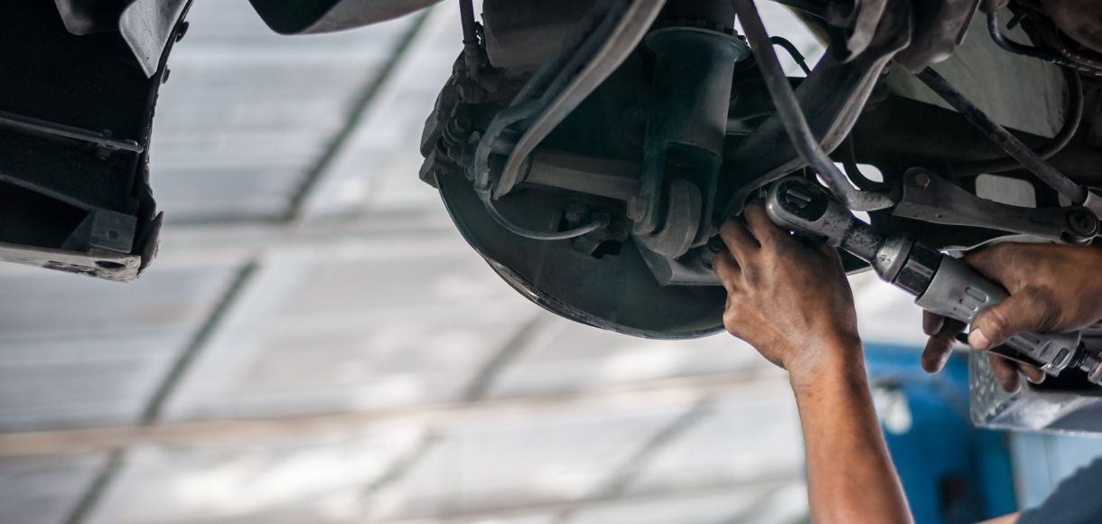 Mechanicβs hands working under a car in a garage, inspecting the underside with a tool.