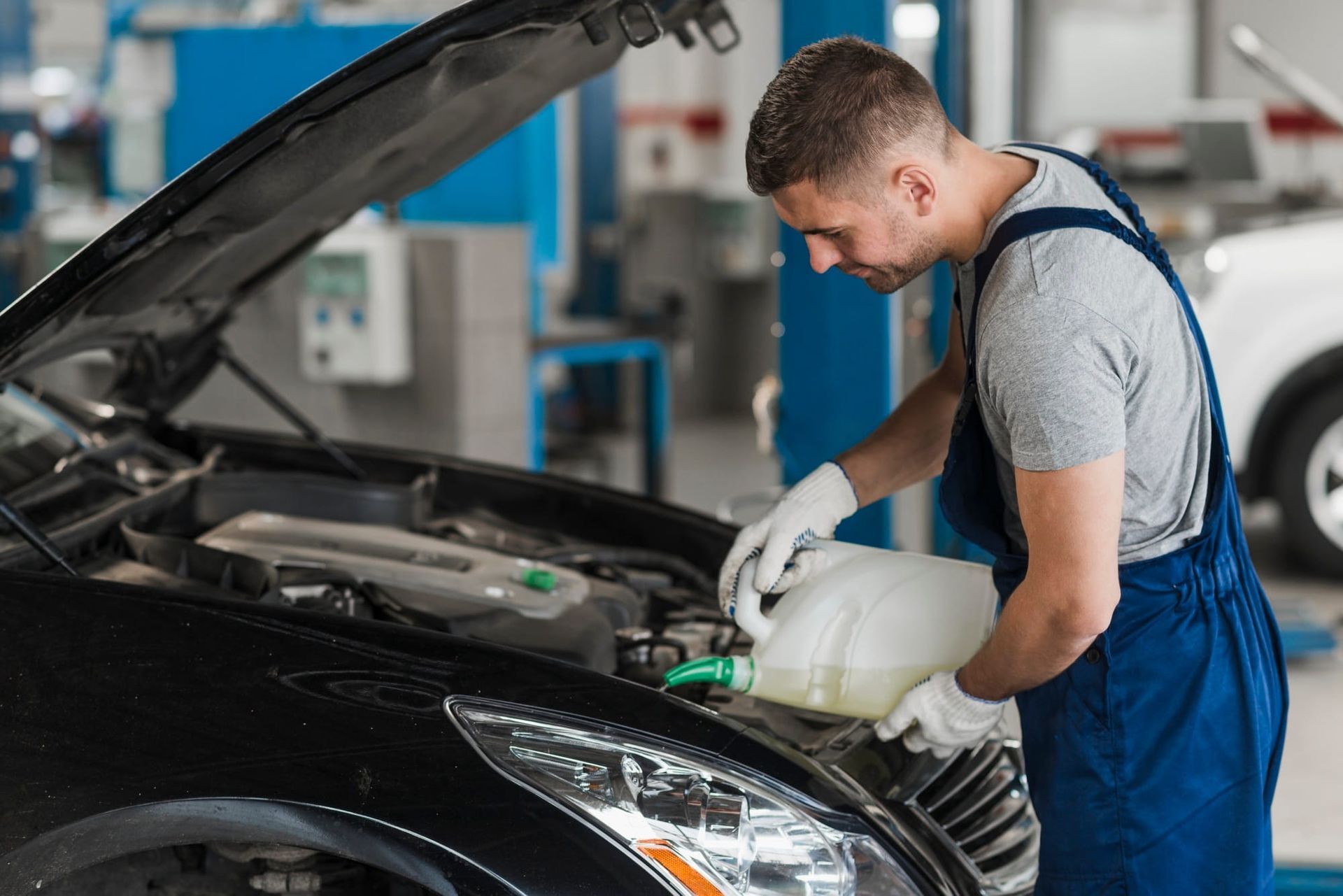 Mechanic in blue overalls checking a black car’s engine in an auto repair shop