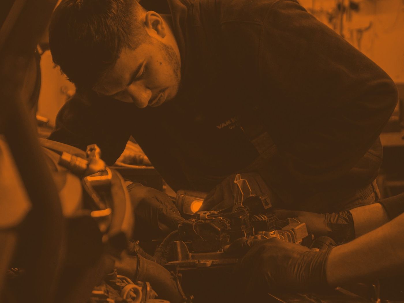 Mechanic inspecting engine components in a dim, orange-lit workshop