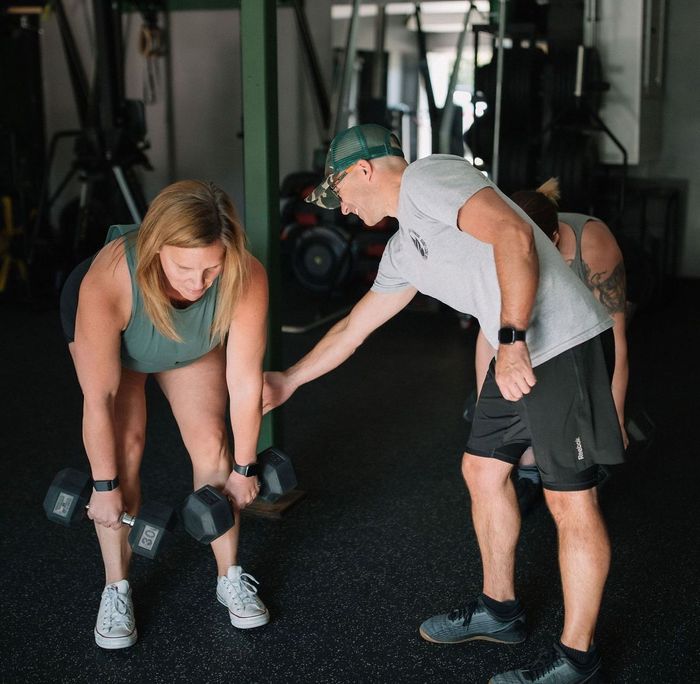 A man is helping a woman lift dumbbells in a gym