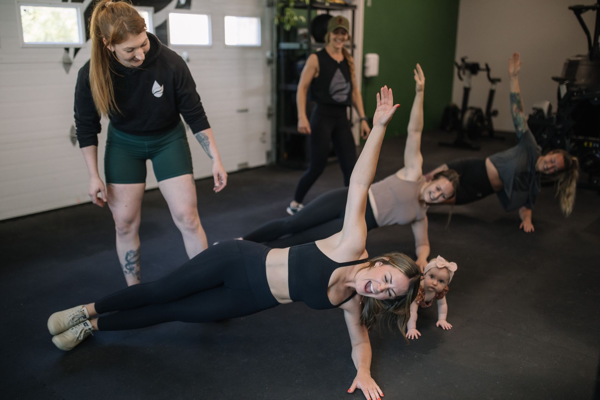 A woman is lifting a barbell in front of a chalkboard with exercises written on it