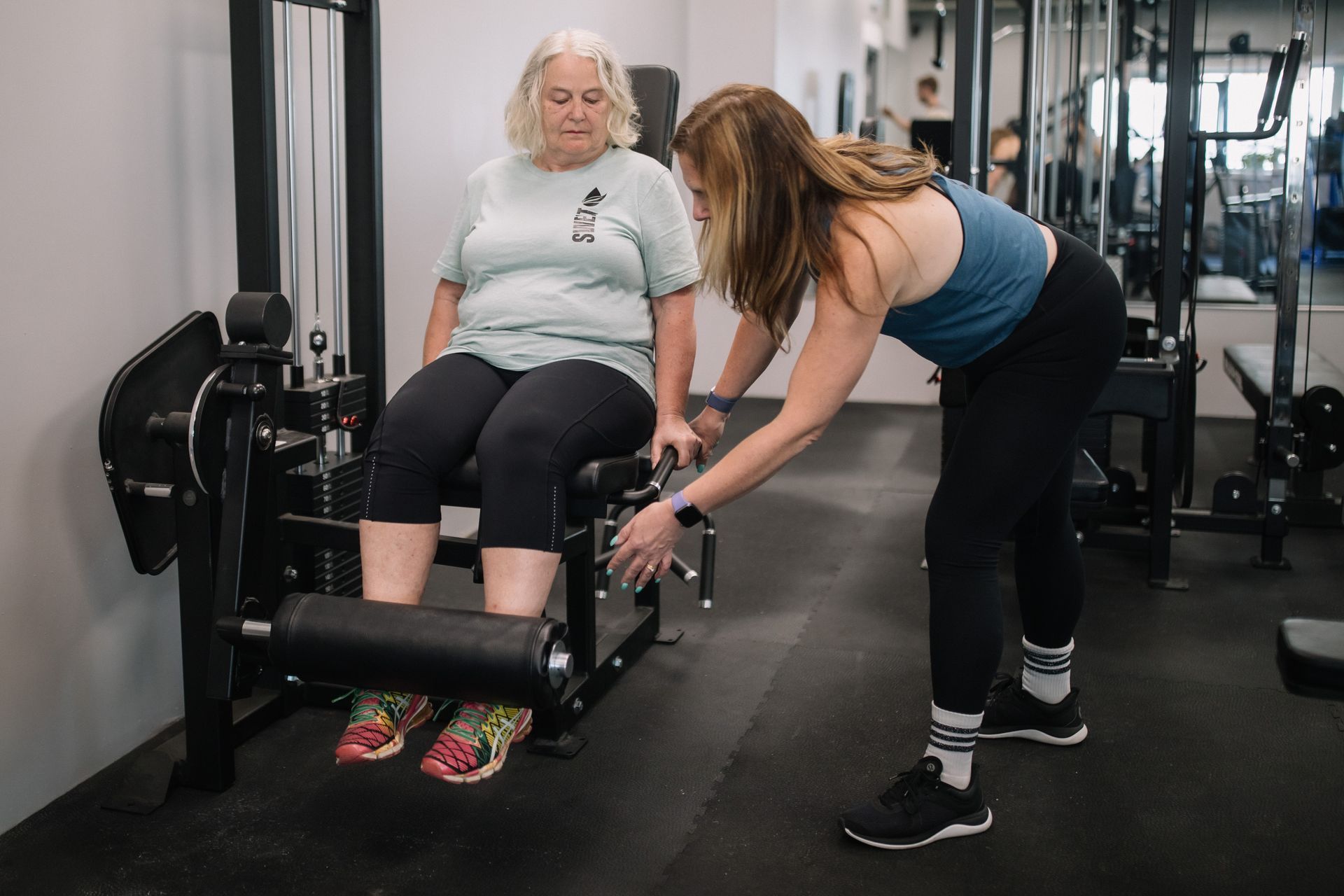A woman is helping another woman use a machine in a gym.