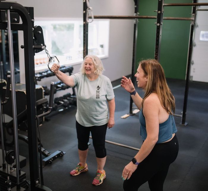 A woman is sitting on a bench lifting dumbbells
