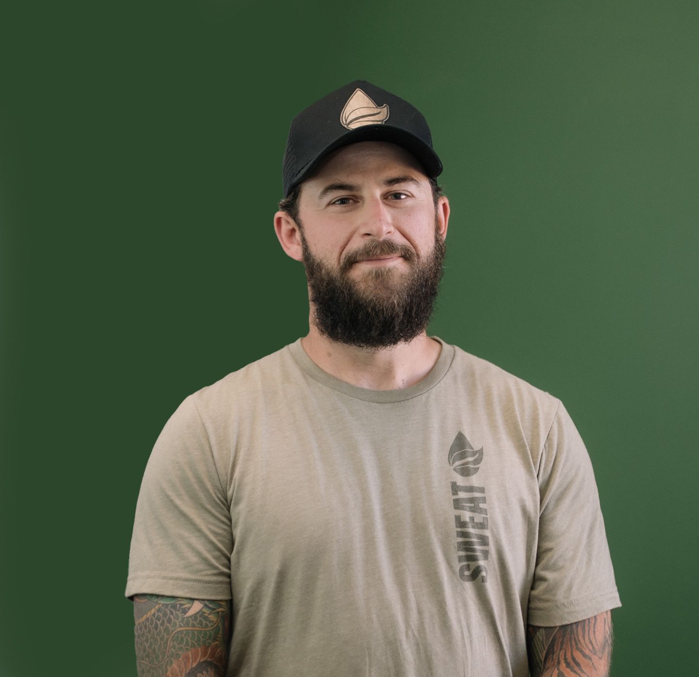 A man with a beard wearing a hat and a shirt that says sweat