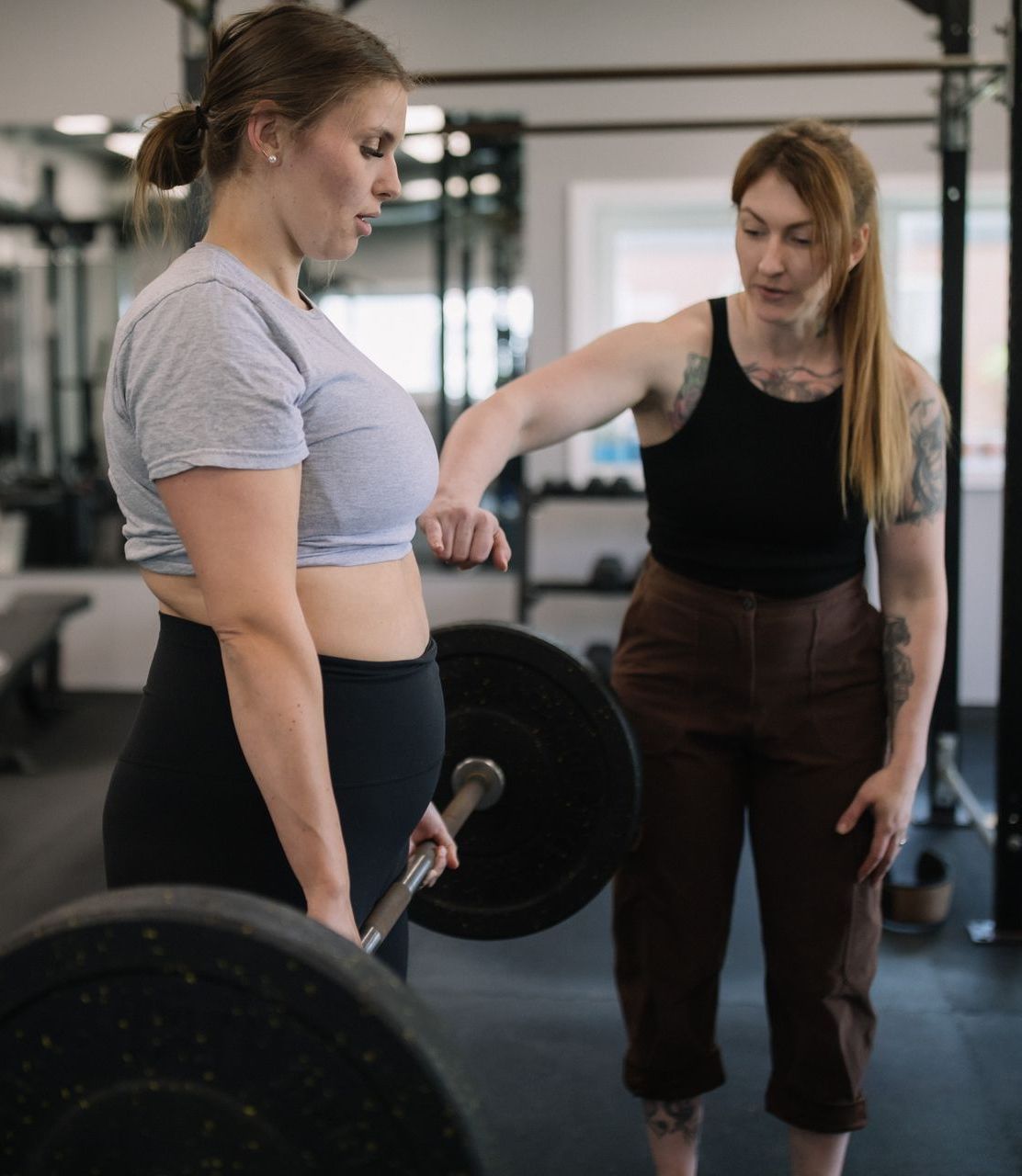 A woman is helping another woman lift a barbell in a gym