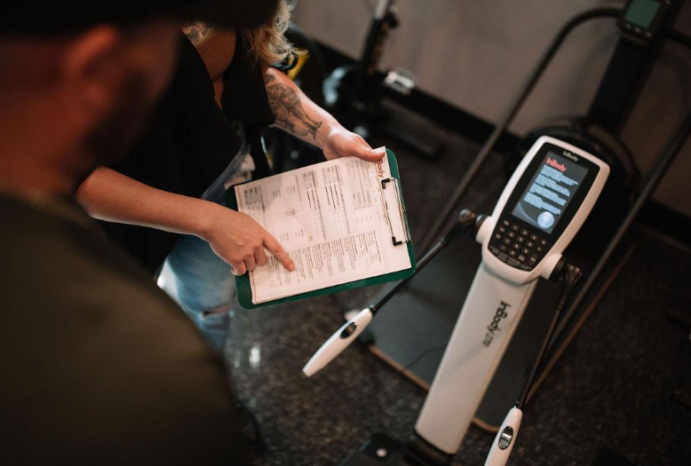 A woman is talking to a man while holding a clipboard in front of a machine.