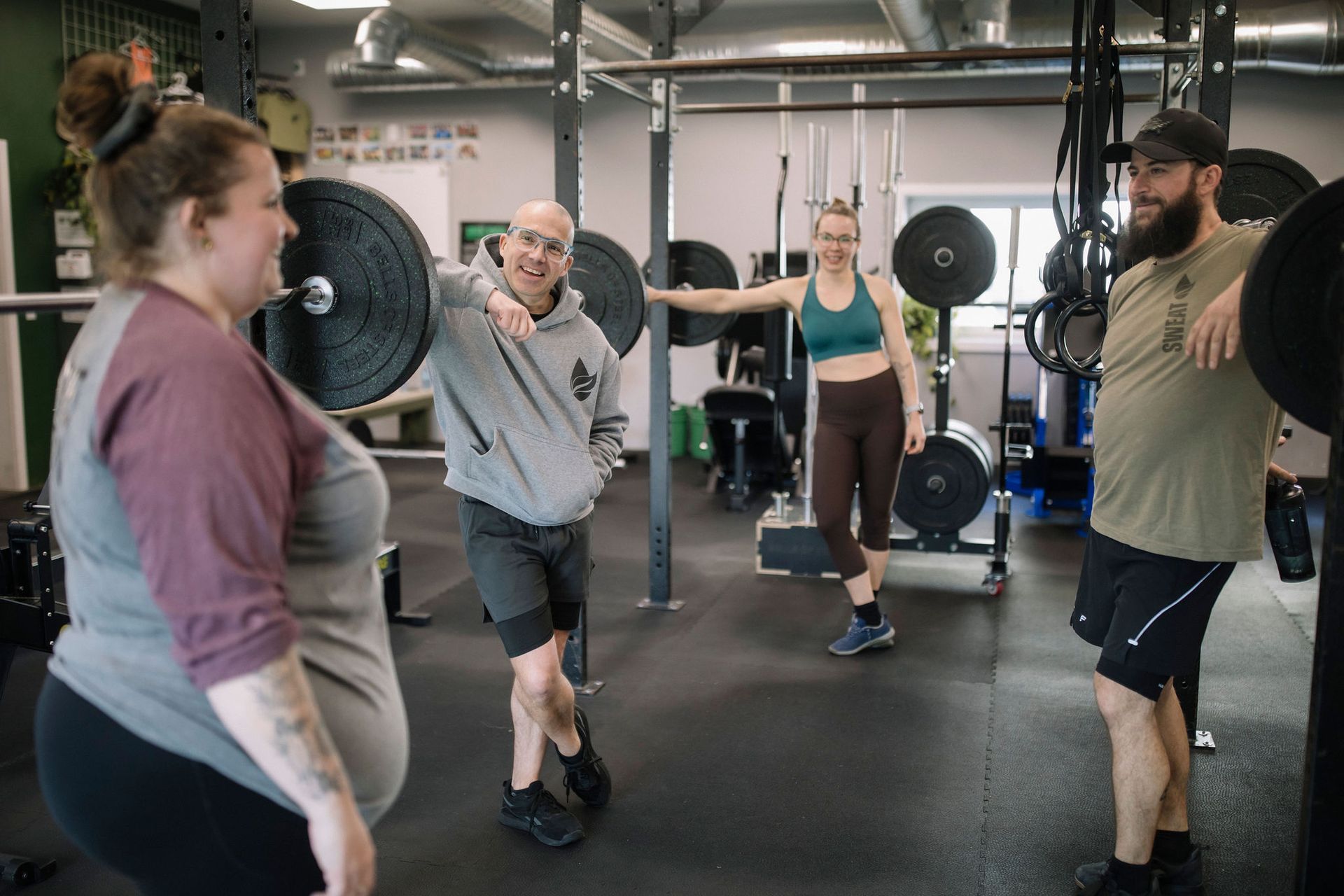 A woman is lifting a barbell in front of a chalkboard with exercises written on it