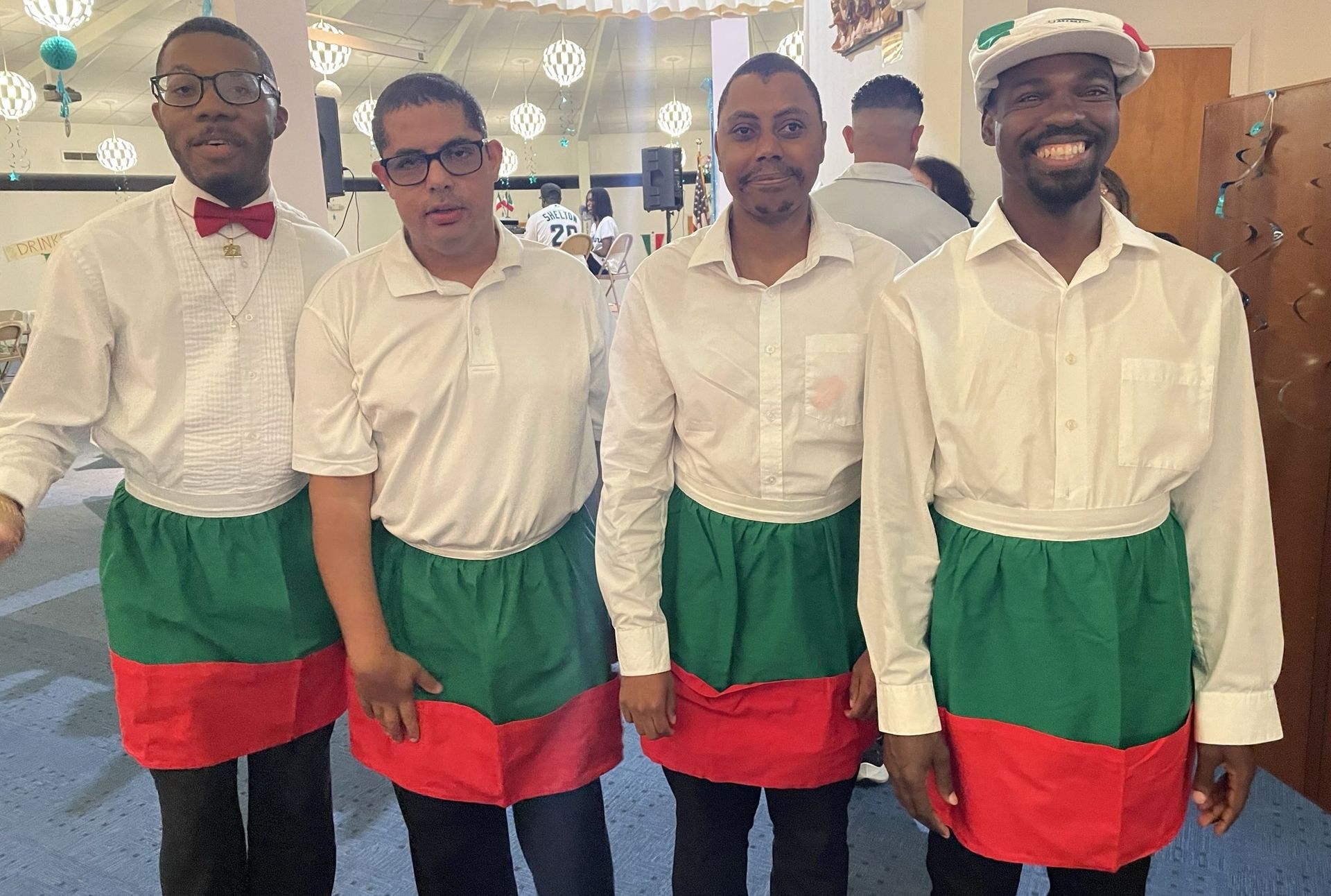 Four men wearing aprons and white shirts are standing next to each other.