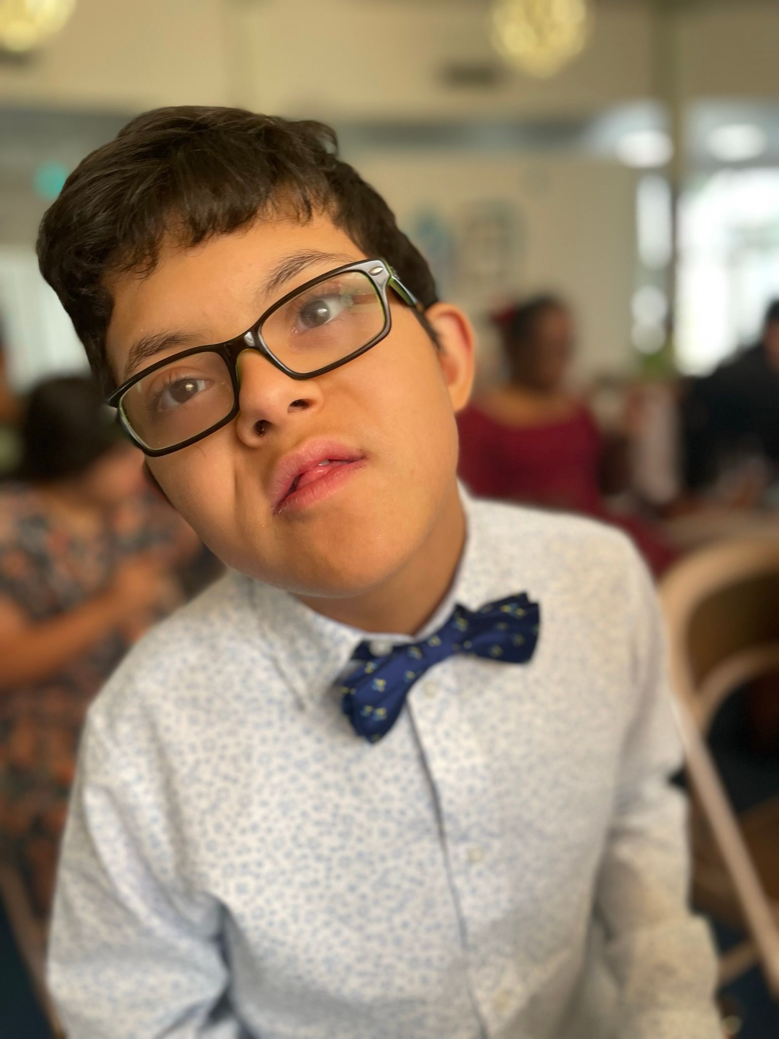 A young boy wearing glasses and a bow tie looks at the camera.