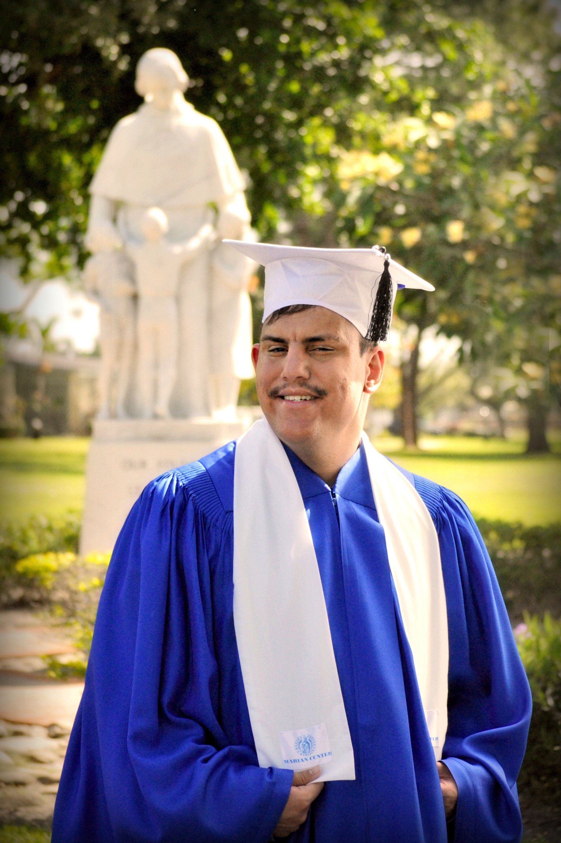 A man in a graduation cap and gown is standing in front of a statue.