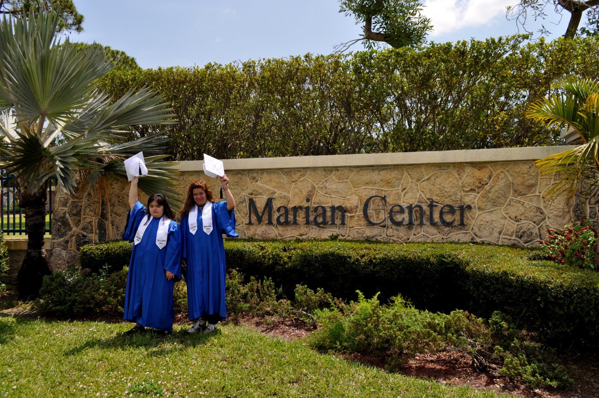 Two women in blue gowns are standing in front of a sign that says marian center