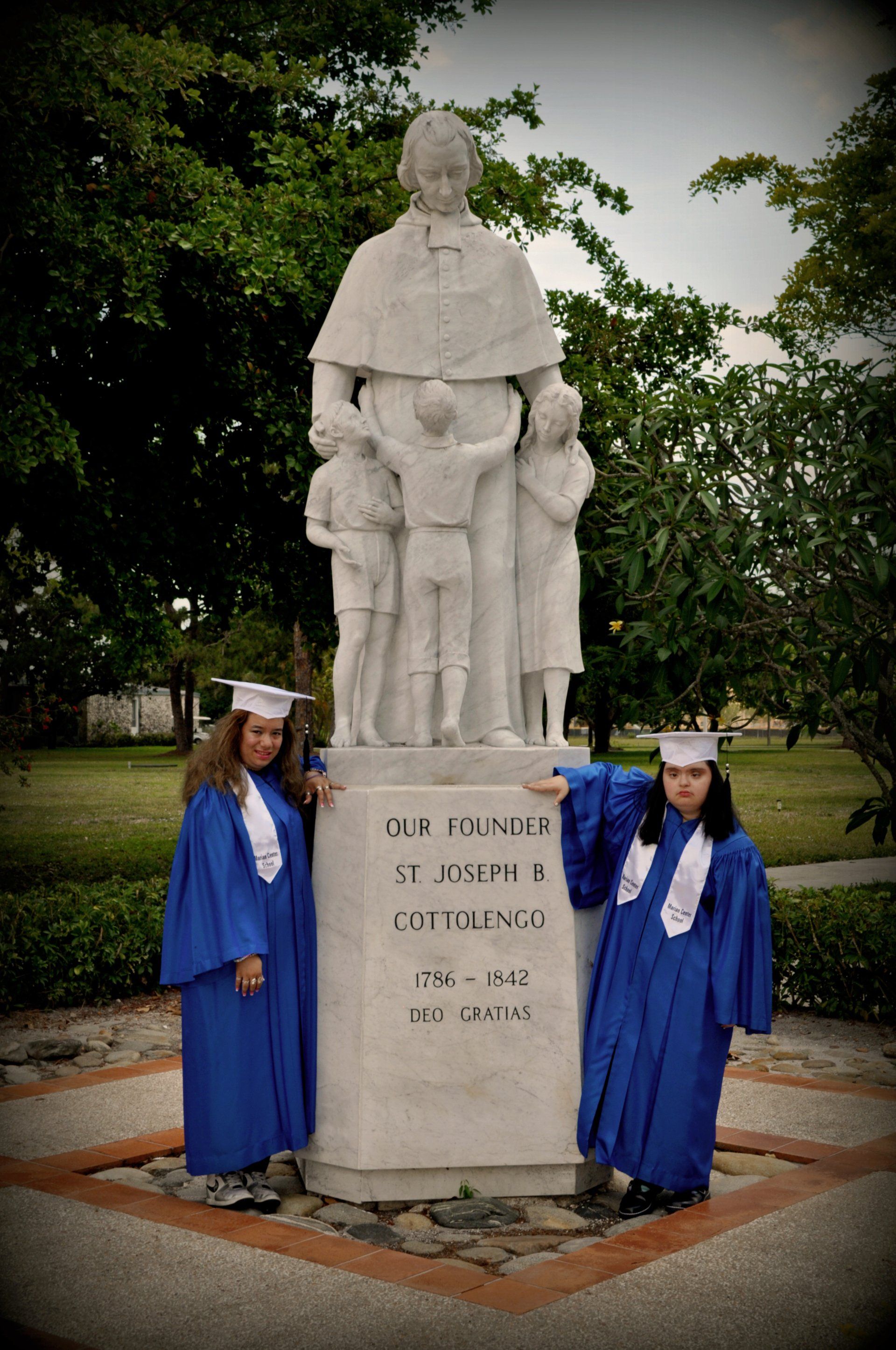 Two girls in graduation gowns pose in front of a statue